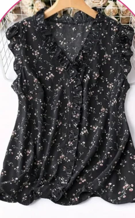 Black sleeveless blouse with a small floral print and ruffle trim on a hanger