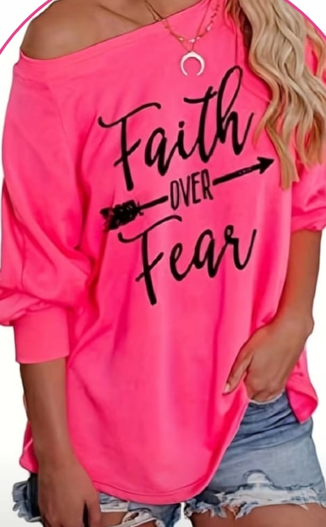 Model wearing a pink off-shoulder sweatshirt printed with the words Faith Over Fear